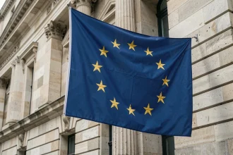 Drapeau européen à douze étoiles dorées accroché à la façade d'un bâtiment officiel en pierre, symbole de l'Union européenne